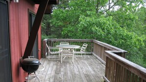 Un terrazzo in legno con tavolo e sedie, un barbecue e vista sugli alberi.