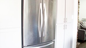 Un refrigerador de acero inoxidable en una cocina con armarios blancos y piso de madera.