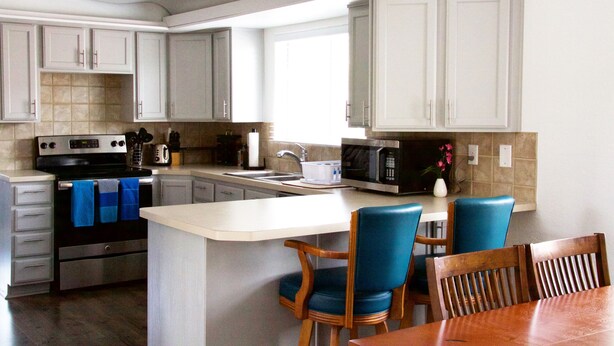 Una cocina moderna con armarios blancos, una isla central, sillas azules y una mesa de comedor de madera.