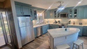 A modern kitchen with blue cabinets, stainless steel appliances, and a central island with stools. - Spacious Waterfront Home In Thousand Islands! (Ogdensburg)