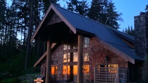 A log cabin with a large porch, multiple windows, and a grill area. - Contemporary Oceanfront Cottage with Private Beaches, Trails, and Gardens (Sooke)