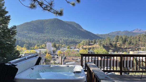 A hot tub on a wooden deck with a view of a town and mountains in the background. - In the center of town with views of Longs Peak (Estes Park)