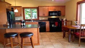 A kitchen with wooden cabinets, a black refrigerator, a microwave, and a dishwasher. There is a dining table with chairs and a window with a view of greenery outside. - 1 BR guest house overlooking a beautiful vineyard  (oliver)