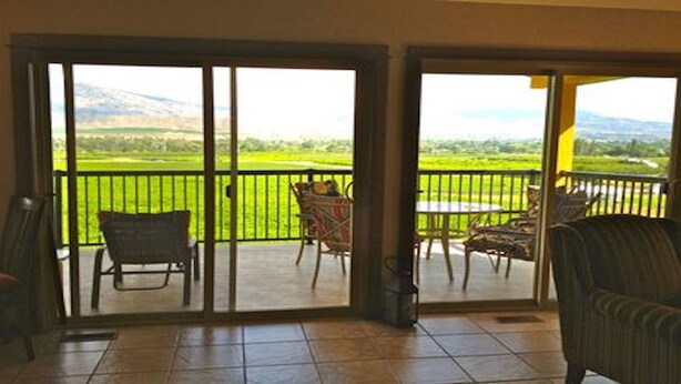 A room with a view of a green field and mountains through large glass doors. There are two chairs and a table on the balcony. - 1 BR guest house overlooking a beautiful vineyard  (oliver)