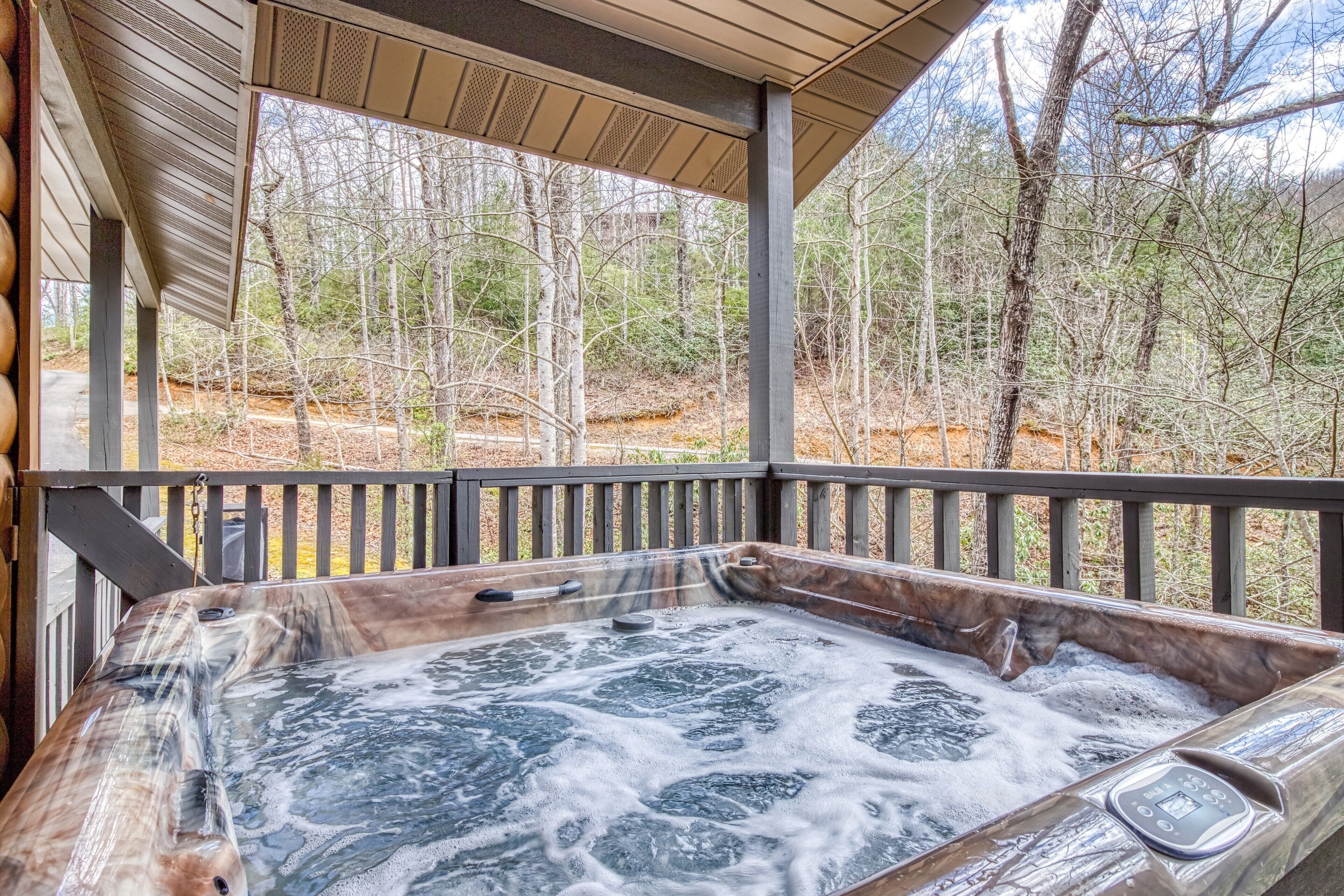 Un bain à remous avec une terrasse en bois et une vue sur une zone boisée.