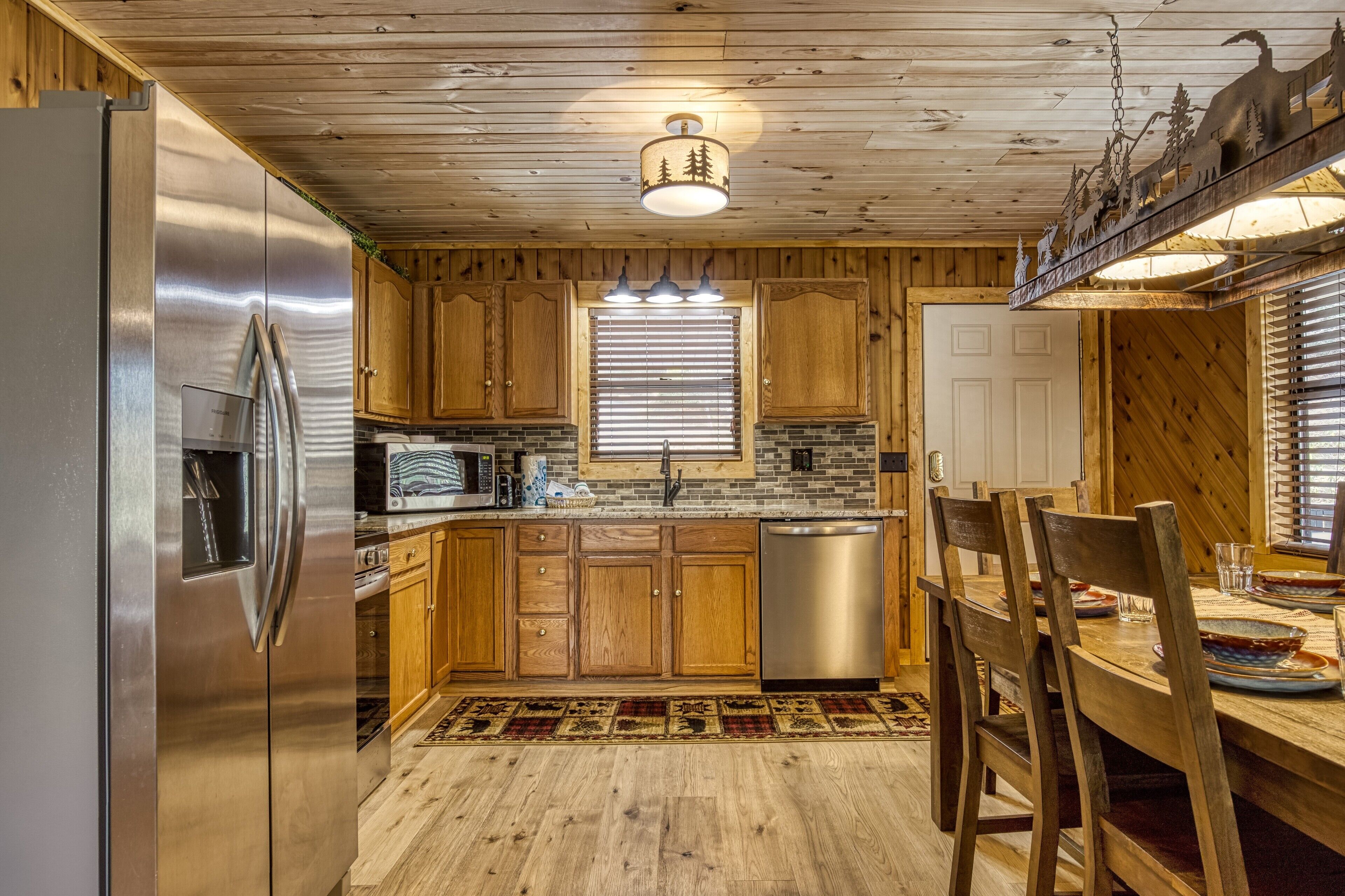 Eine holzgetäfelte Küche im Chalet-Stil mit einem Edelstahlkühlschrank, Holzschränken, einem Geschirrspüler und einem Essbereich mit Holztisch und Stühlen.