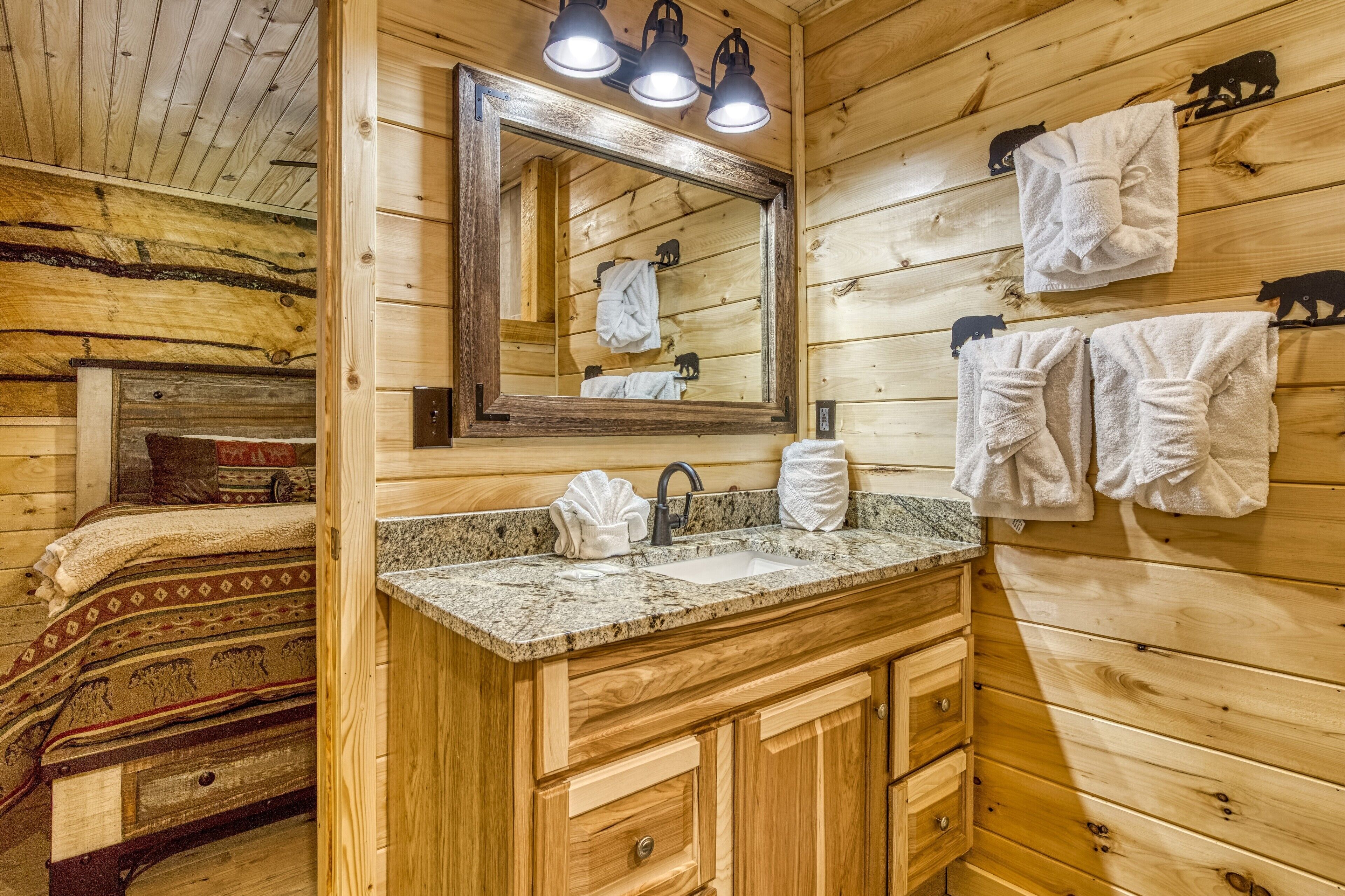 Un baño tipo cabaña de madera con encimera de granito, armarios de madera, un espejo grande y toallas colgadas en la pared.