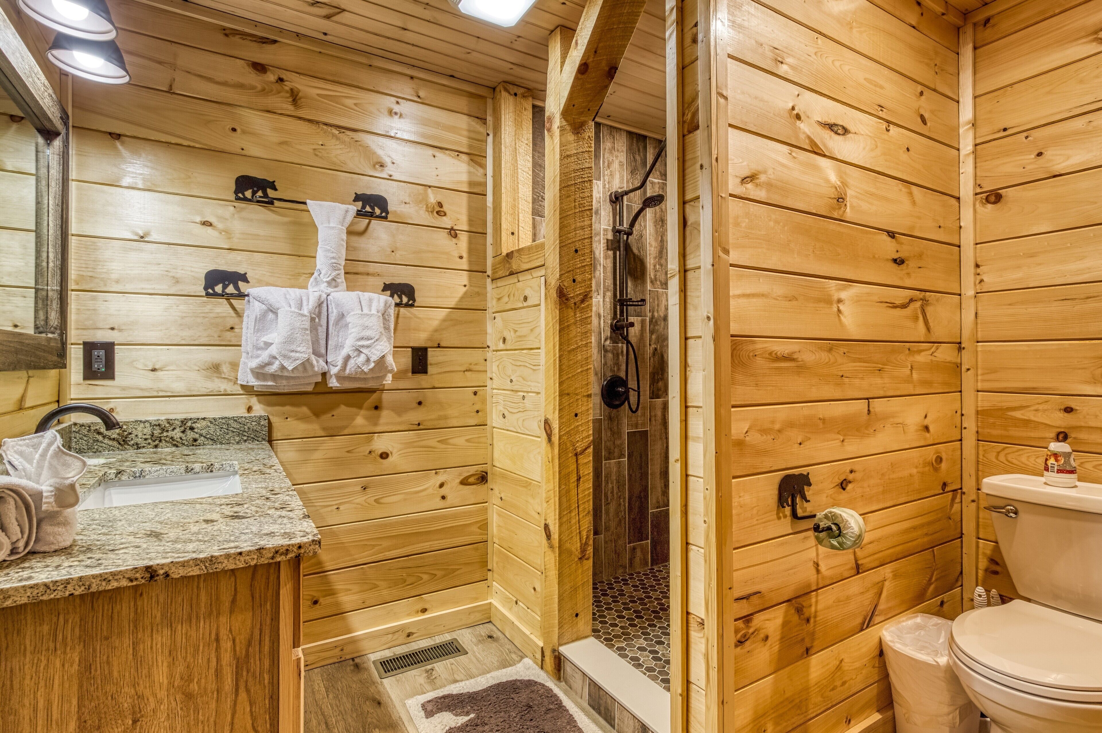 Baño de cabaña de madera con lavamanos, toallero, ducha e inodoro.