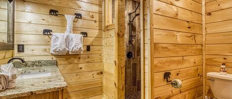 Baño de cabaña de madera con lavamanos, toallero, ducha e inodoro.