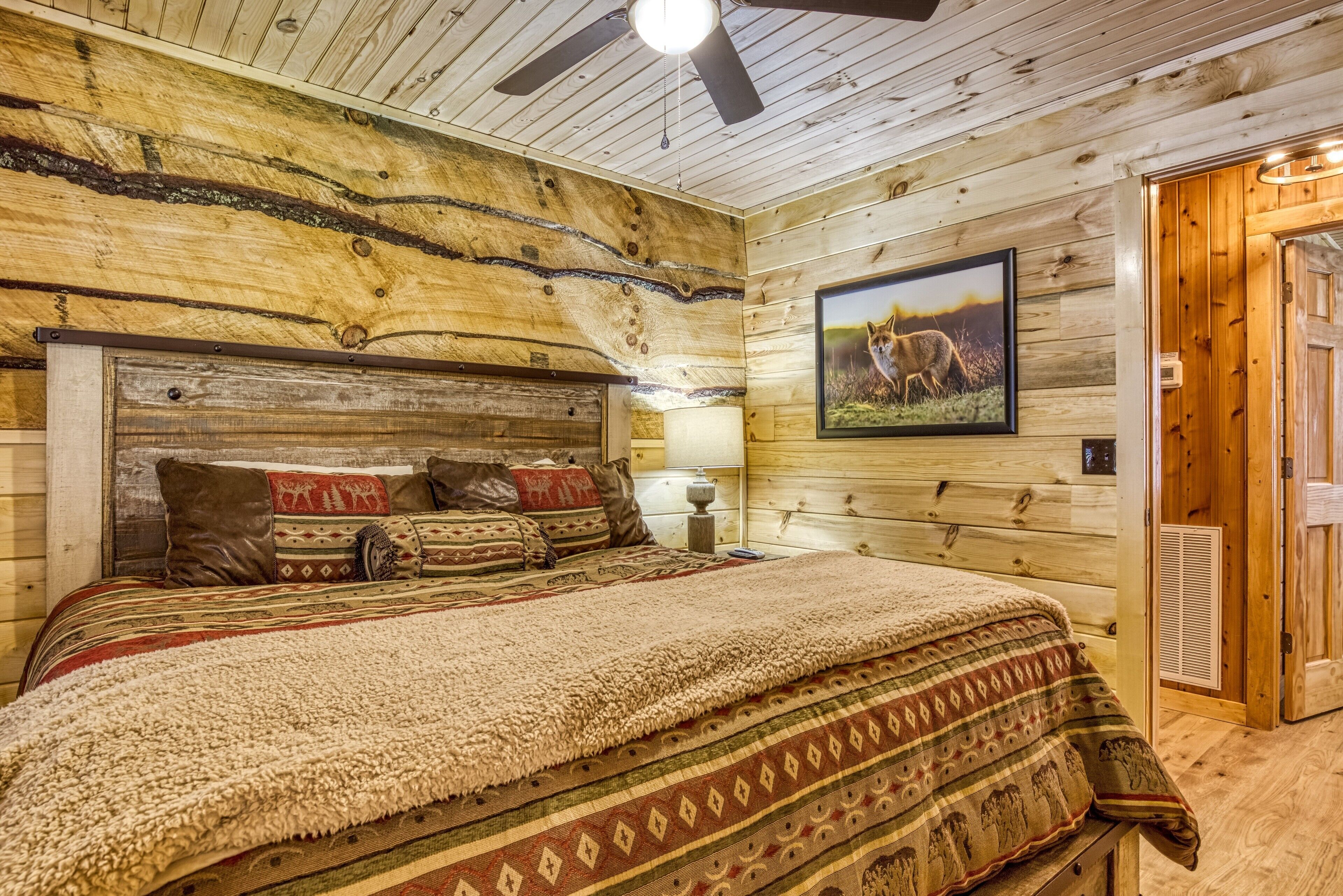Ein Schlafzimmer einer Holzhütte mit einem Bett, Kissen, einem gerahmten Bild und einem Deckenventilator.