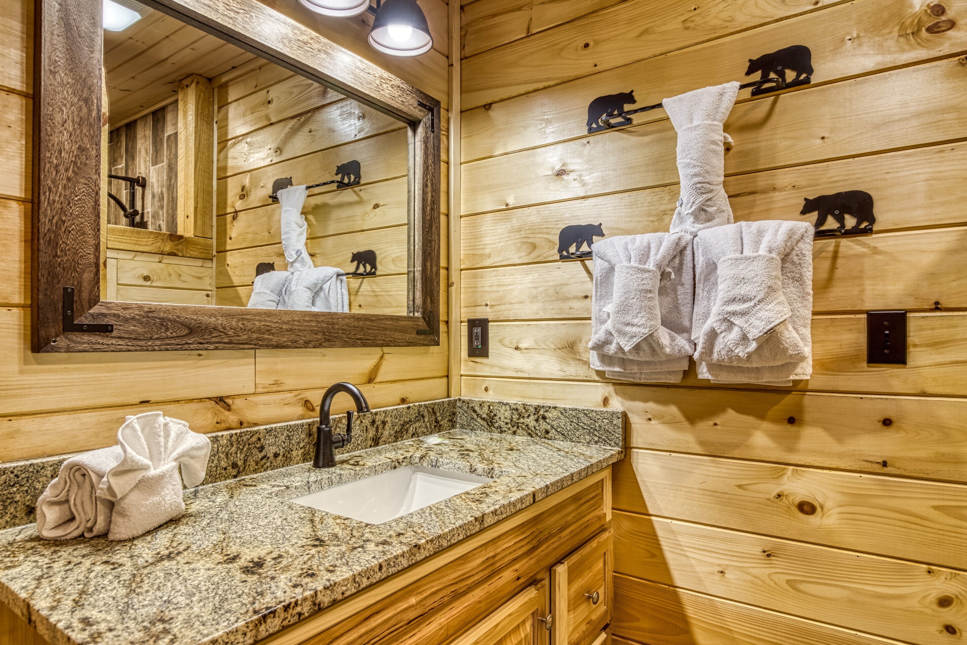 Une salle de bain rustique, avec une cabine en bois, un lavabo en granit, des meubles en bois, un miroir et des porte-serviettes décorés de motifs d’ours.