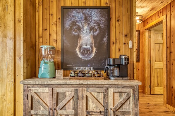 A wooden cabin interior with a rustic bar area featuring a blender, coffee maker, and a framed picture of a dog.