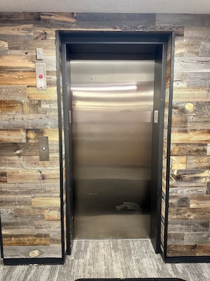 Un ascensor con interior metálico, flanqueado por paredes de paneles de madera con diseño rústico.