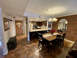 Una cocina con una isla central, sillas de madera oscura, una mesa de comedor y una pared de ladrillo.