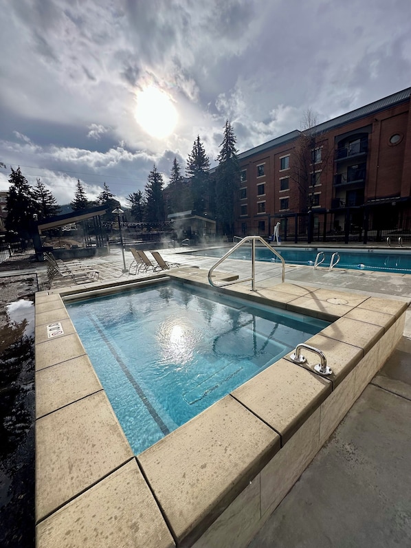 A rectangular pool with a hot tub, surrounded by a tiled deck.