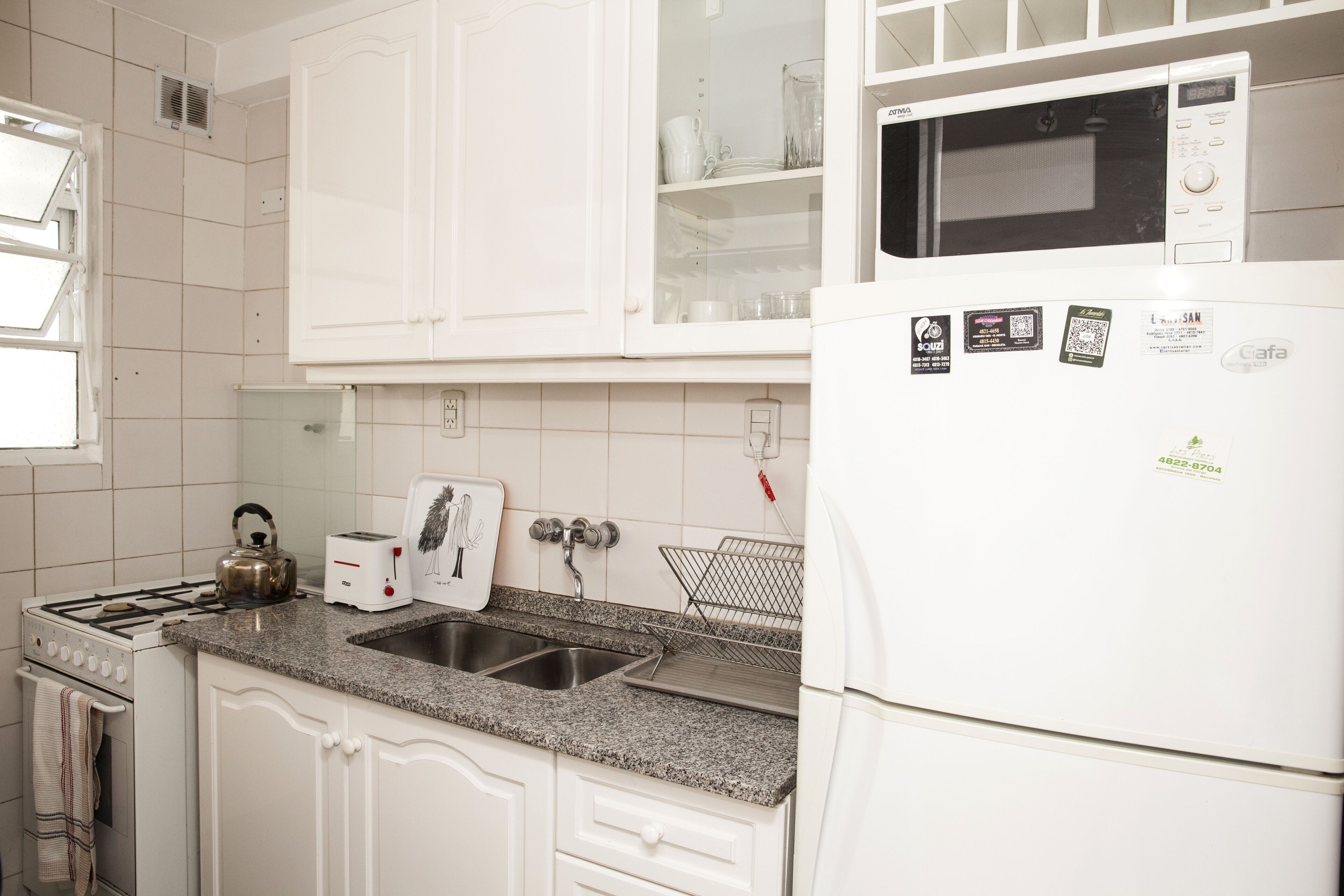 Een keuken met witte kastjes, een granieten aanrecht, een fornuis, een spoelbak, een magnetron en een koelkast.