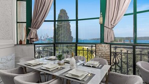 Comedor con una mesa dispuesta para cuatro, ventanas amplias con cortinas y vista a una formación rocosa distante.