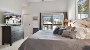 Een slaapkamer met een groot bed, een dressoir, een televisie en een balkon met uitzicht op het landschap.