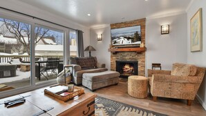 Een gezellige woonkamer met een open haard, comfortabele zitplaatsen en een groot raam met uitzicht op een besneeuwd terras.
