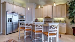 Una cocina moderna con armarios blancos, electrodomésticos de acero inoxidable y taburetes de bar.