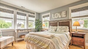 A bedroom with a large bed, two bedside tables, a nightstand, a dresser, and a window with blinds.