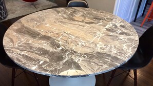 Una mesa redonda de comedor con cubierta de mármol, rodeada por cuatro sillas negras.