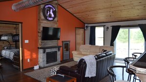 A living room with a fireplace, a television, a sofa, and a dining area. - Controlled Chaos Basecamp - centered between Jackson & Clark County Trail System (Merrillan)