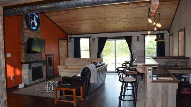 A spacious living area with a fireplace, a sofa, and a bar area with stools. - Controlled Chaos Basecamp - centered between Jackson & Clark County Trail System (Merrillan)