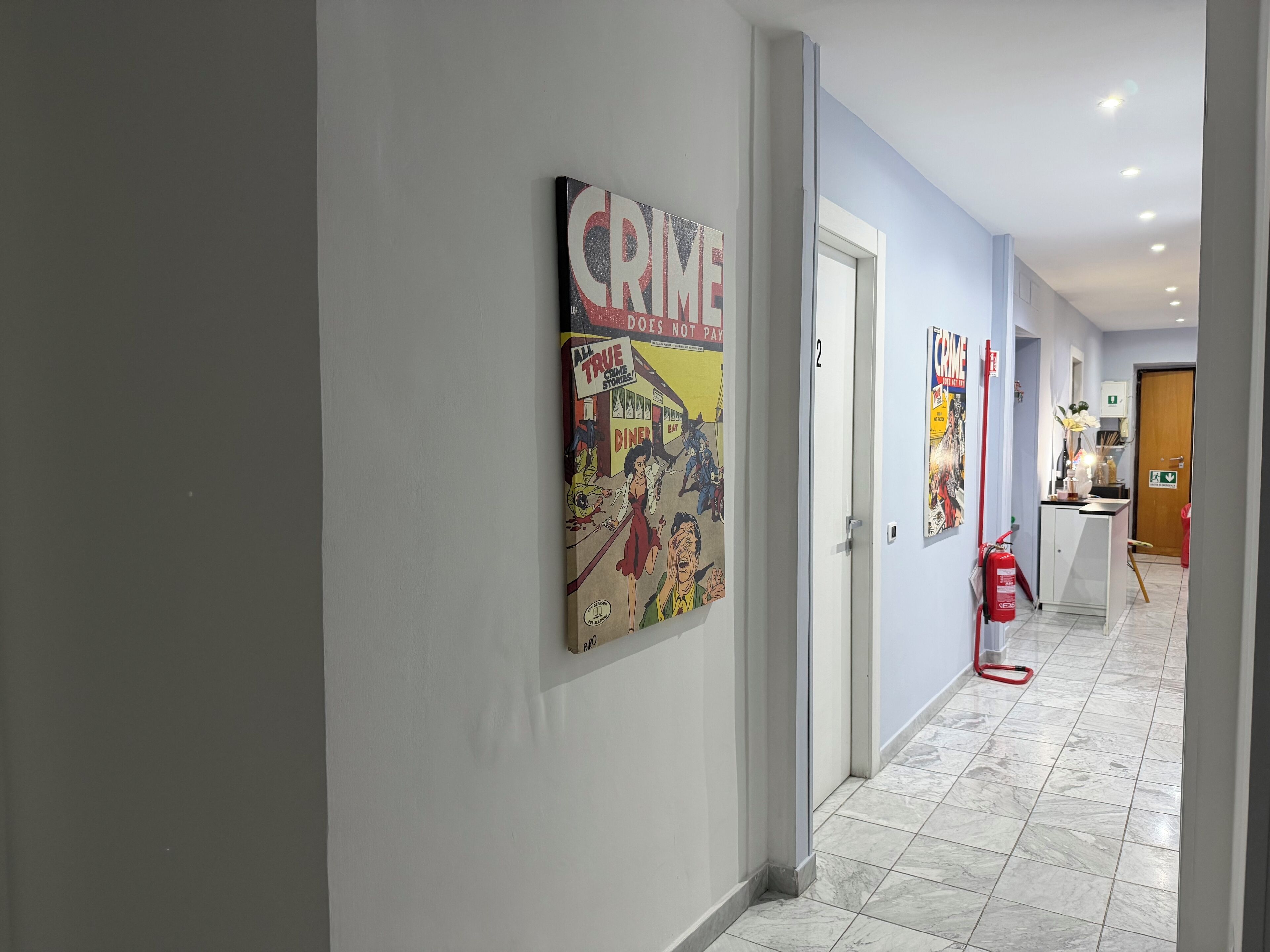 Un couloir avec une affiche de bande dessinée sur le thème de « Le crime ne paie pas », un extincteur et une porte portant le numéro « 2 ».
