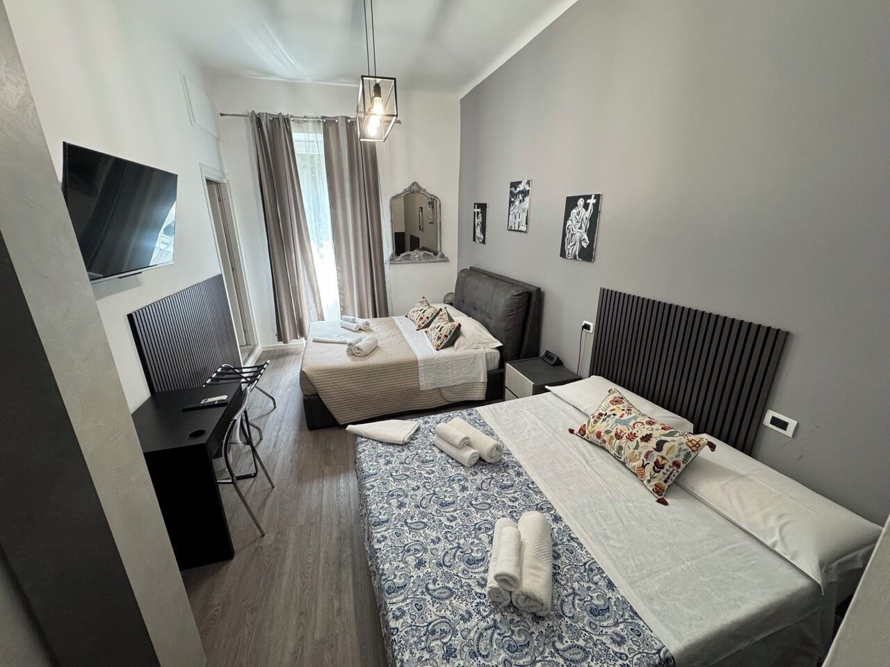 Une chambre d’hôtel moderne, équipée de deux lits, d’un bureau, d’une chaise, d’une télévision et ornée d’œuvres d’art sur les murs.