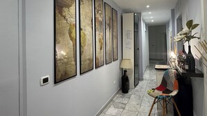 Een gang met inlijstingen van kaarten aan de muur, een lamp, een fles en een stoel.