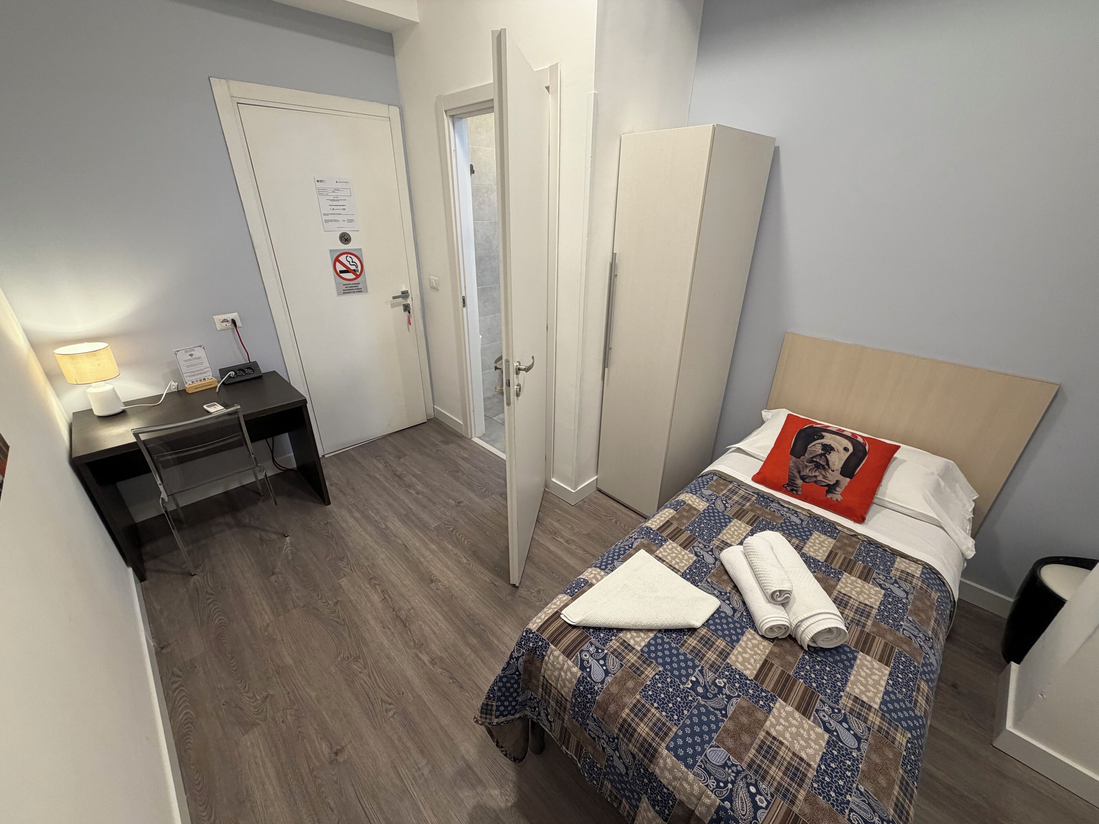 A hotel room with a bed, a desk, a chair, and a wardrobe.