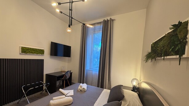 Een moderne hotelkamer met een bed, een bureau, een stoel, een flatscreen televisie en een raam met gordijnen.