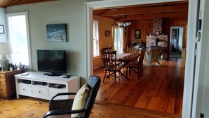 A cozy living room with a television, a dining area with wooden furniture, and a kitchen visible through an open doorway. - Lakefront Home On Beautiful Donnells Pond,32 miles From Acadia N P and Bar Harbr (Franklin)
