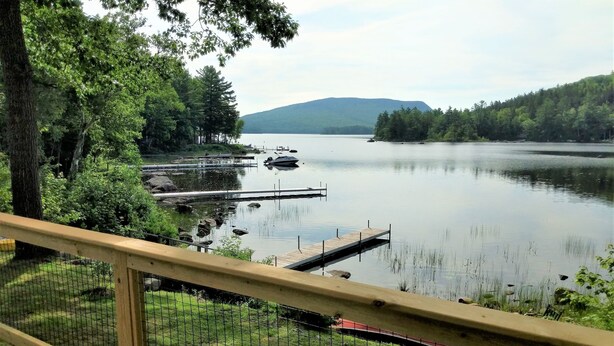 A lakeside view from a deck with a wooden railing, dock, and surrounding greenery. - Lakefront Home On Beautiful Donnells Pond,32 miles From Acadia N P and Bar Harbr (Franklin)