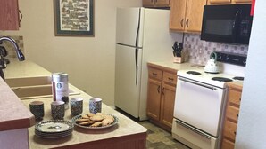 A kitchen with wooden cabinets, a refrigerator, a stove, and a microwave. There are mugs and a plate with cookies on the counter.