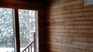 A wooden cabin interior with a hot tub, large windows, and a view of snow-covered trees.