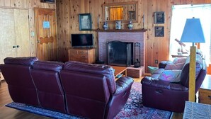 Interior acogedor de una cabaña con chimenea, sofás de cuero y paredes de madera.