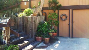 Una escalera de madera que lleva a la entrada de un edificio, con un cartel con el número 364, plantas en macetas y una corona en la puerta.