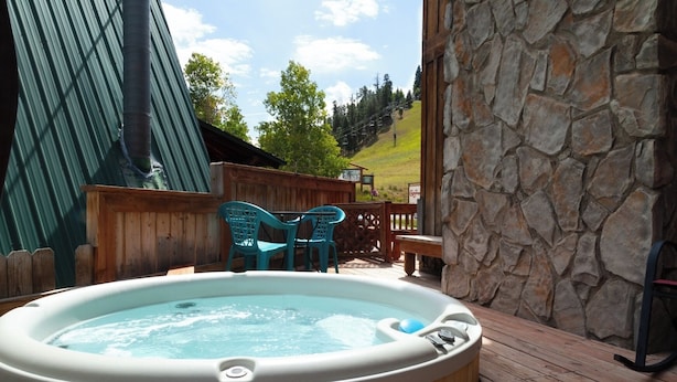A hot tub on a wooden deck with a stone wall and a view of a ski lift in the background.