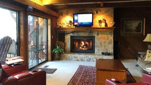 A cozy living room with a stone fireplace, a television on a wooden shelf, and red leather sofas. - FALLING WATERS ~ 2b/2b SPECTACULAR VIEW HANGING OVER FALLS, UPSCALE FURNISHINGS. (Lake Toxaway)