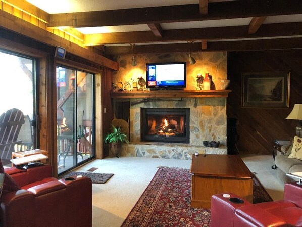 A cozy living room with a stone fireplace, a television on a wooden shelf, and red leather sofas. - FALLING WATERS ~ 2b/2b SPECTACULAR VIEW HANGING OVER FALLS, UPSCALE FURNISHINGS. (Lake Toxaway)