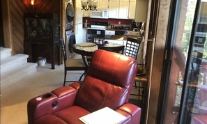 A red leather chair with a notebook, a dining table with chairs, a kitchen with white cabinets, and a view through a glass door. - FALLING WATERS ~ 2b/2b SPECTACULAR VIEW HANGING OVER FALLS, UPSCALE FURNISHINGS. (Lake Toxaway)