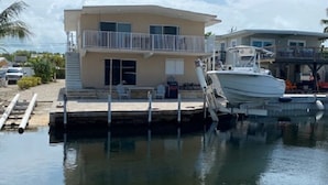 Una casa de dos pisos con balcón, un barco amarrado y un cielo despejado.