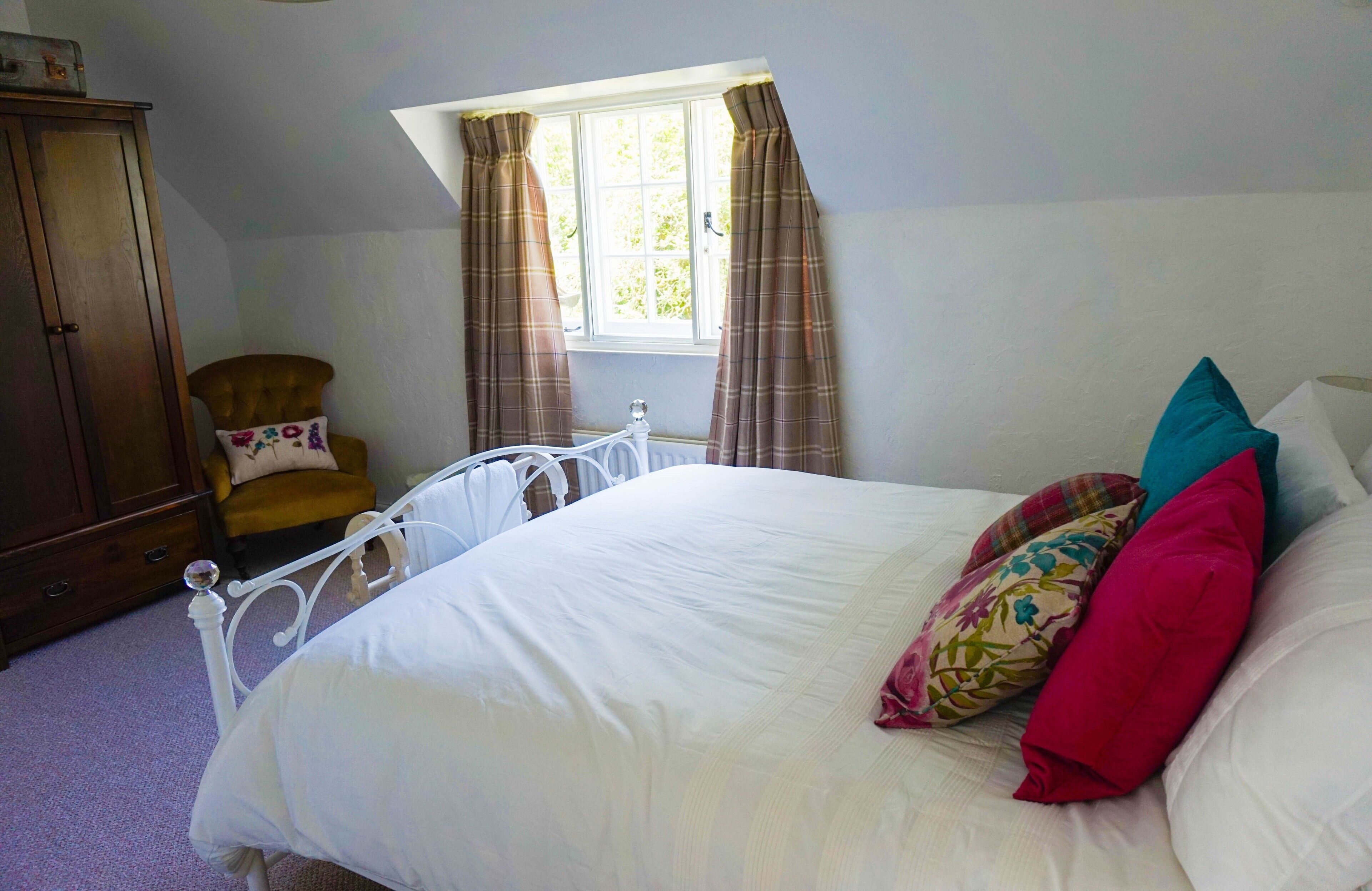 Un dormitorio con cama, una silla, un armario y una ventana con cortinas.