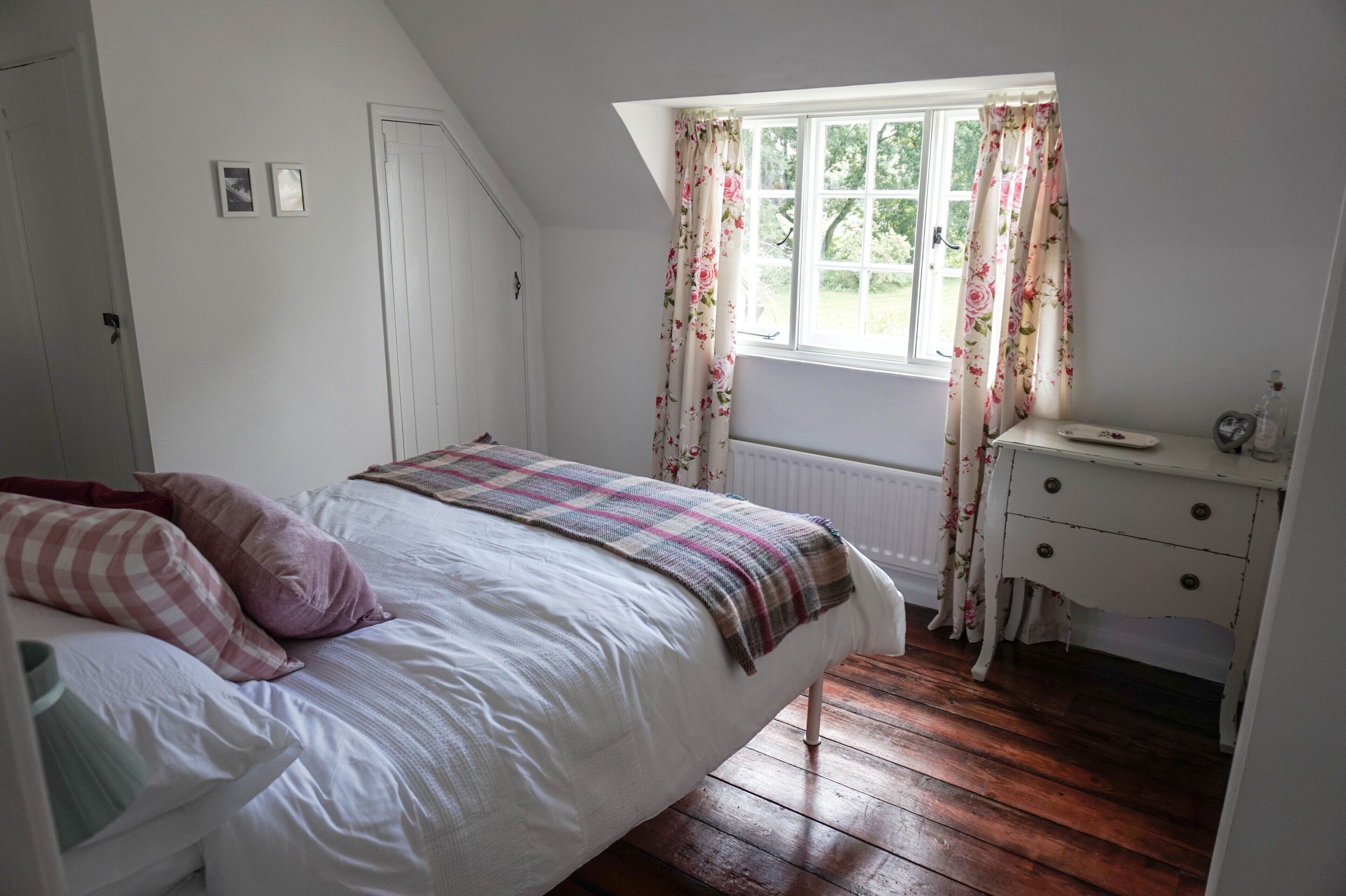 A bedroom with a bed, a dresser, a window with floral curtains, and a radiator.