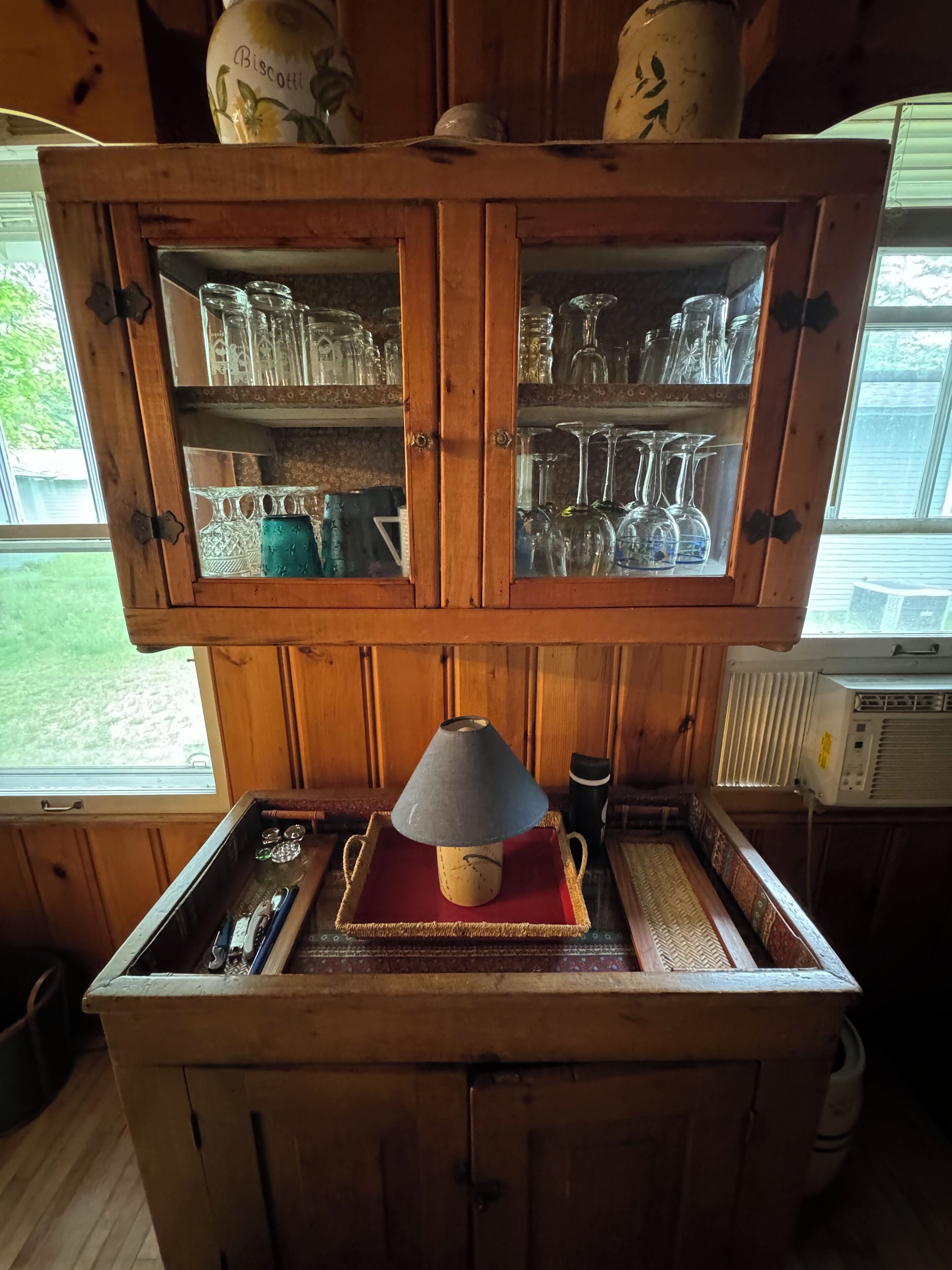 Un meuble en bois doté de portes en verre, contenant divers objets en verre et une lampe posée sur un plateau.