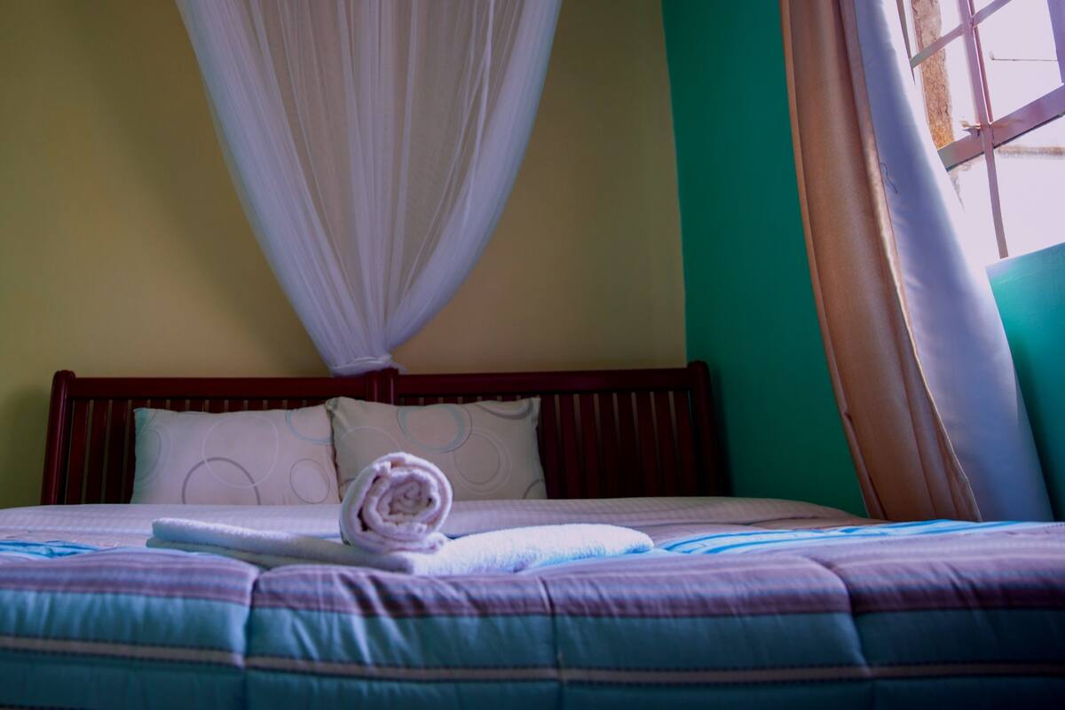 A neatly made bed with a striped bedspread, a rolled towel, and a white canopy.