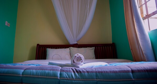 A neatly made bed with a striped bedspread, a rolled towel, and a white canopy.