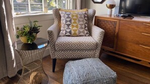 Un salón acogedor con un sillón estampado, una mesita auxiliar con una planta y un mueble de madera con un televisor.
